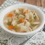 Homemade chicken noodle soup with carrots and celery in a white bowl on a lace and green napkin.