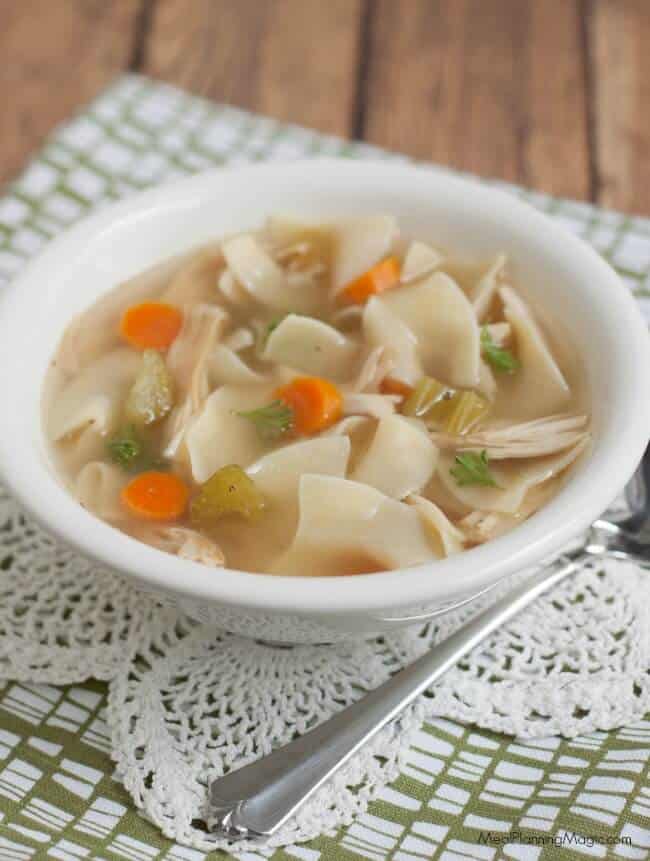 Homemade chicken noodle soup with carrots and celery in a white bowl on a lace and green napkin.