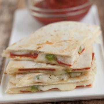 Stack of triangle shaped Pizza Quesadillas on a plate with marinara sauce in a bowl.