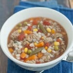 Top view image of slowcooker ground turkey, mixed vegetable and barley soup on a blue napkin with spoon on side.