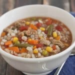 image of slowcooker ground turkey, mixed vegetable and barley soup in a white bowl on blue napkin with spoon.