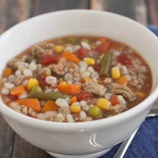 image of slowcooker ground turkey, mixed vegetable and barley soup in a white bowl on blue napkin with spoon.