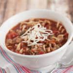 Crockpot Lasagna Soup with shredded cheese on top in a white bowl on a blue and white napkin