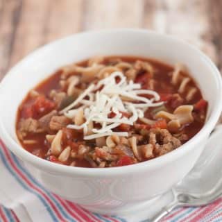 Crockpot Lasagna Soup with shredded cheese on top in a white bowl on a blue and white napkin