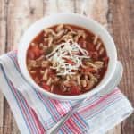 Top view image of Crockpot Lasagna Soup with shredded cheese on top in a white bowl on a blue and white napkin