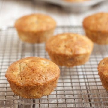 Image of banana muffins placed on a cooling rack with muffin tin in background.