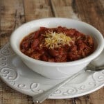 side view image of slowcooker classic American chili with beans topped with shredded cheddar cheese in a white bowl on a white plate