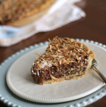 Slice of German Chocolate Sweet Cream Pie on white plate and blue plate with whole pie in background.