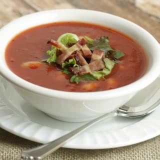 Bacon, lettuce, tomato and beans soup in a white bowl on white plate with spoon.