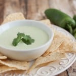 Creamy Jalapeno Ranch Dip in a white bowl with sprig of cilantro on top and tortilla chips and large jalapeno on side.