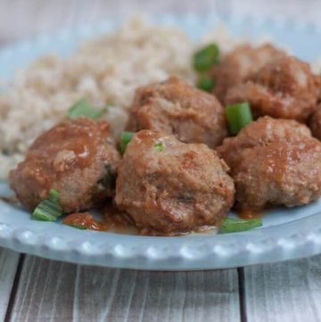 Closeup view of several peachy ground turkey meatballs with minced green onion garnish and rice pilaf on a blue plate.