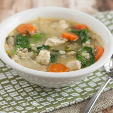 Bowl of Roasted Vegetables, Chicken and Rice soup on a green and white napkin with spoon.