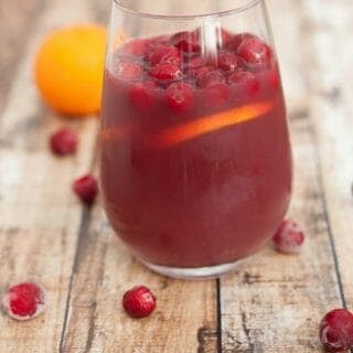 Cranberry Orange Sangria in a glass with cranberries and orange slice floating at top and whole orange at upper left of glass.
