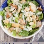 image of romaine lettuce salad with bow-tie pasta, croutons, chicken and shaved Parmesan cheese in a blue and white bowl