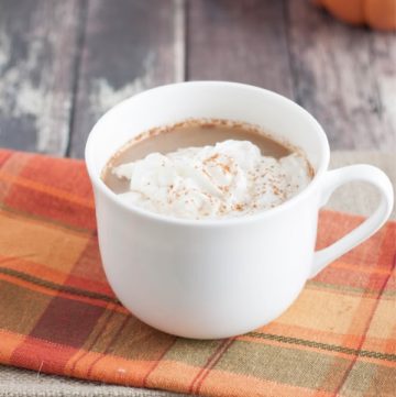 Side view image of Pumpkin Spice Latte Creamer in mug with orange checkered fabric and pumpkins.