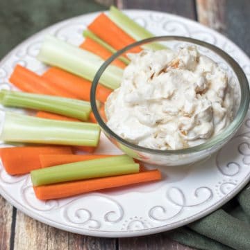 Image of Homemade French Onion Dip in a bowl with pieces of carrot and celery on a plate.