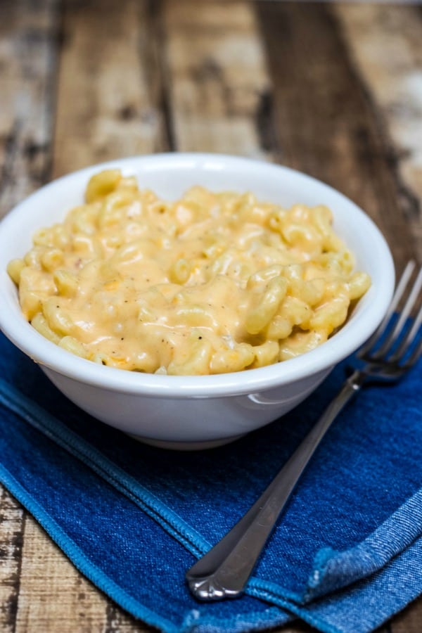 Image of homemade macaroni and cheese in a bowl on top of a napkin with fork on side. 