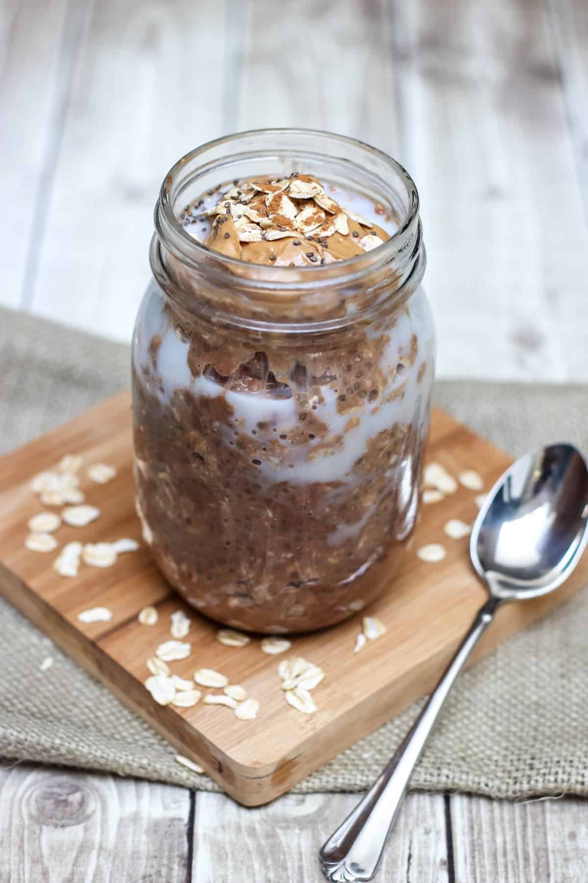 Glass jar containing ingredients mixture of Cinnamon Chocolate Peanut Butter Overnight Oats.