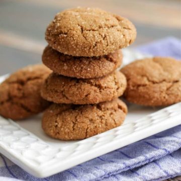Stack of soft and chewy molasses ginger cookies on a white plate on top of a blue napkin.