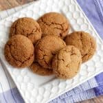 Pile of soft and chewy molasses ginger cookies on a square white plate on top of a blue napkin.
