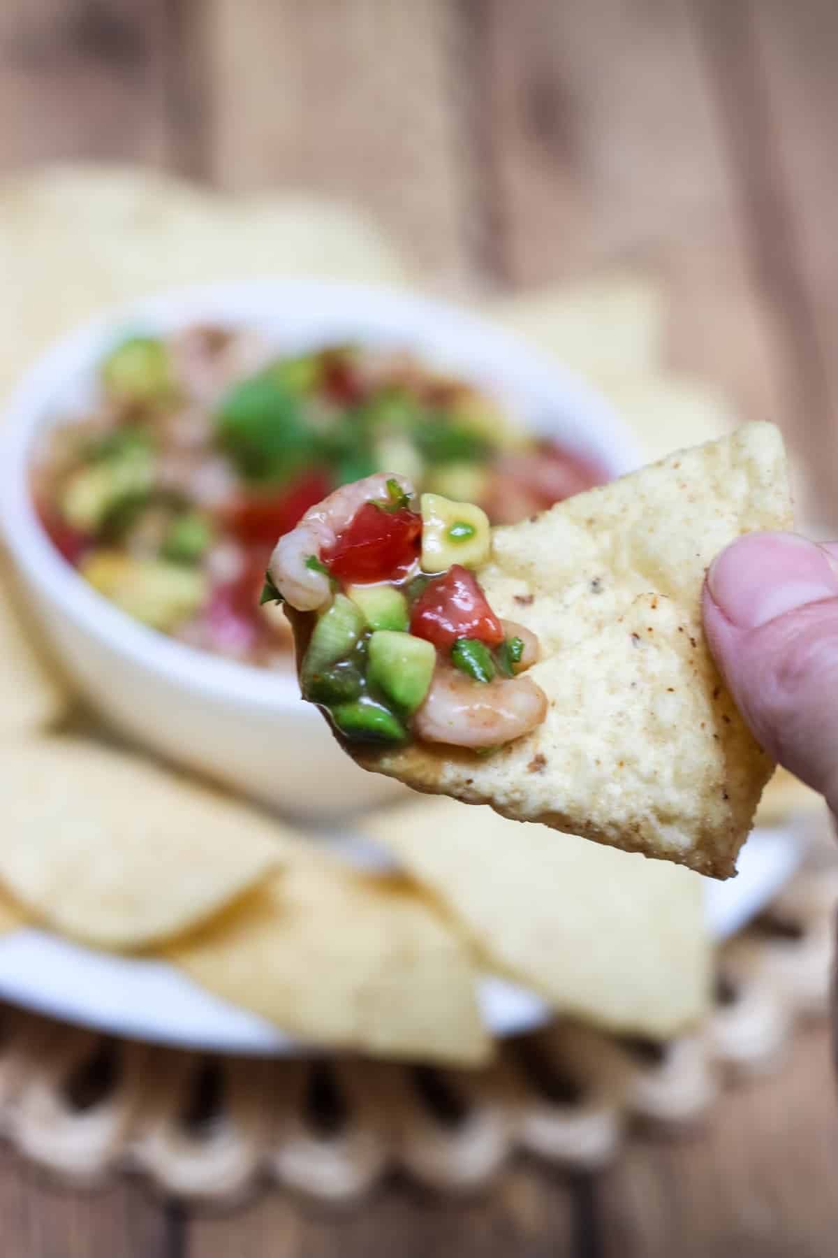 Shrimp Avocado Salsa close up on a tortilla chip with bowlful in background. 
