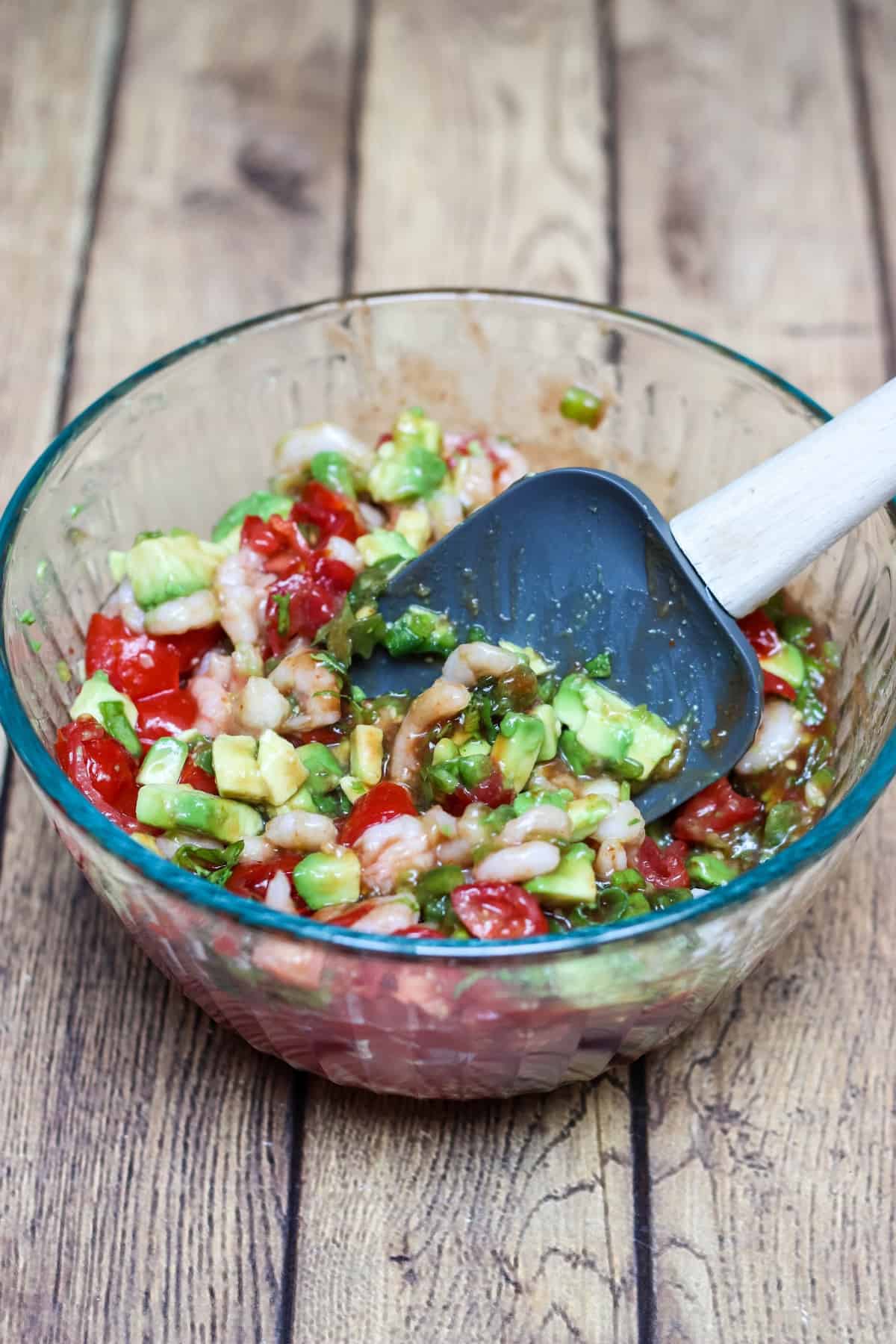 Ingredients for Shrimp Avocado Salsa in a glass bowl being mixed with rubber spatula. 