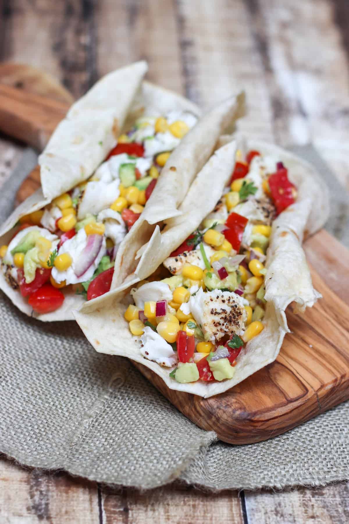 image of white fish with corn, tomato and avocado salsa in tortilla on cutting board.
