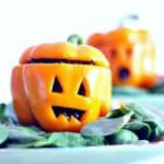 Orange bell pepper with Jack O Lantern face carved in it on a blue-green napkin