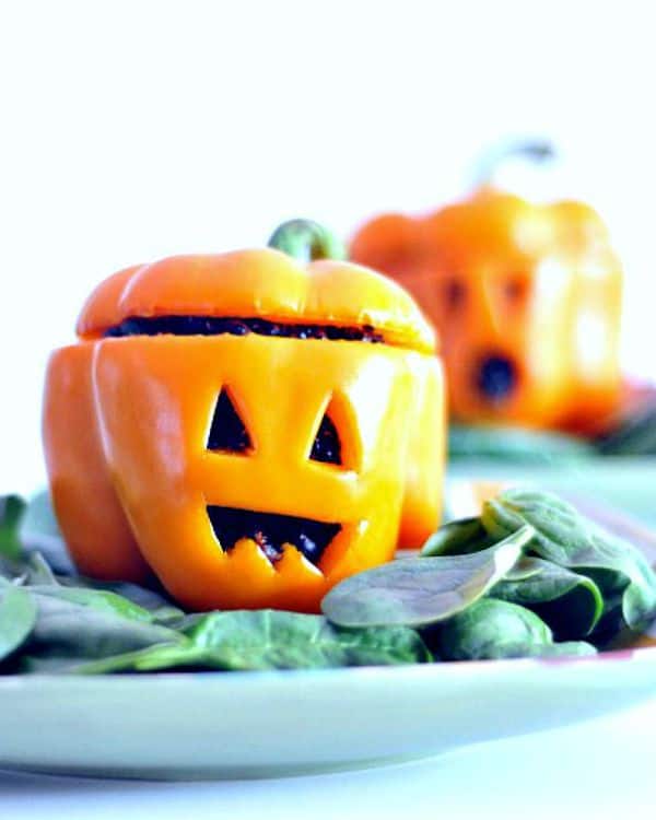 Orange bell pepper with Jack O Lantern face carved in it on a blue-green napkin