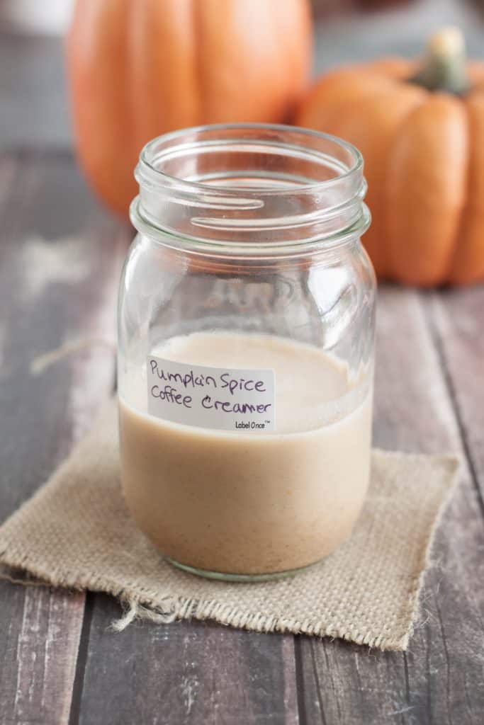 Labeled glass mason jar Pumpkin Spice Coffee Creamer and decorative pumpkins in background.