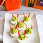 Egg and avocado deviled eggs with red bell pepper slices on a white plate.