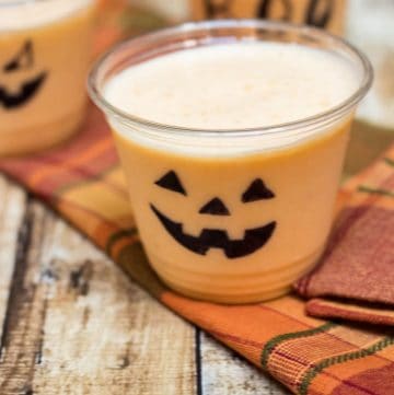 Orange Peach Smoothie in clear cups decorated for Halloween on orange plaid napkin.