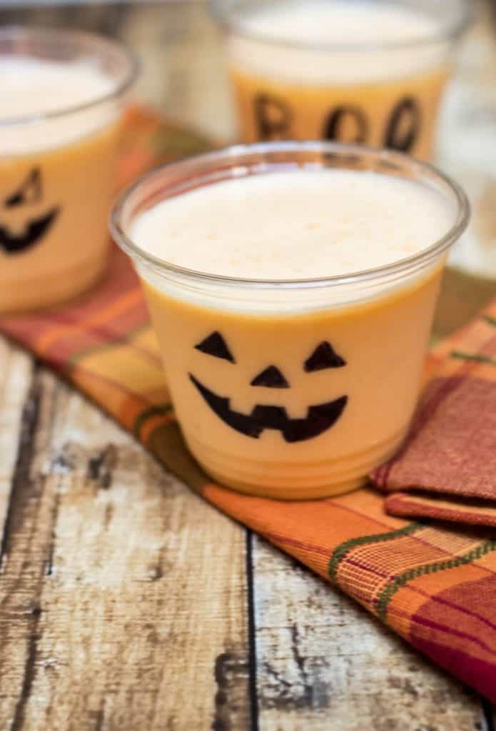 Orange Peach Smoothie in clear cups decorated for Halloween on orange plaid napkin.