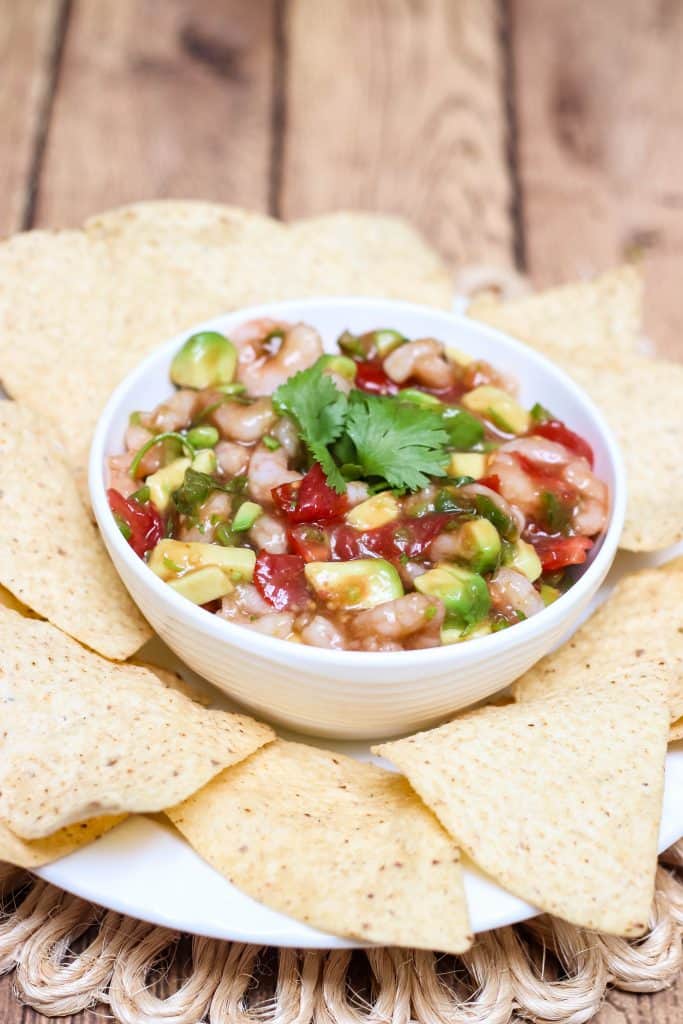 Shrimp avocado salsa in a white bowl with tortilla chips on plate. 