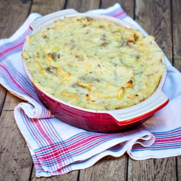 Creamy garlic herb mashed potatoes casserole in a red dish on a blue and white towel.