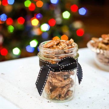 jar with black ribbon containing kahlua sugar pecans and colored lights of Christmas tree in background