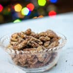 Glass bowl with Kahlua sugared pecans on white counter with lights from Christmas tree in background.