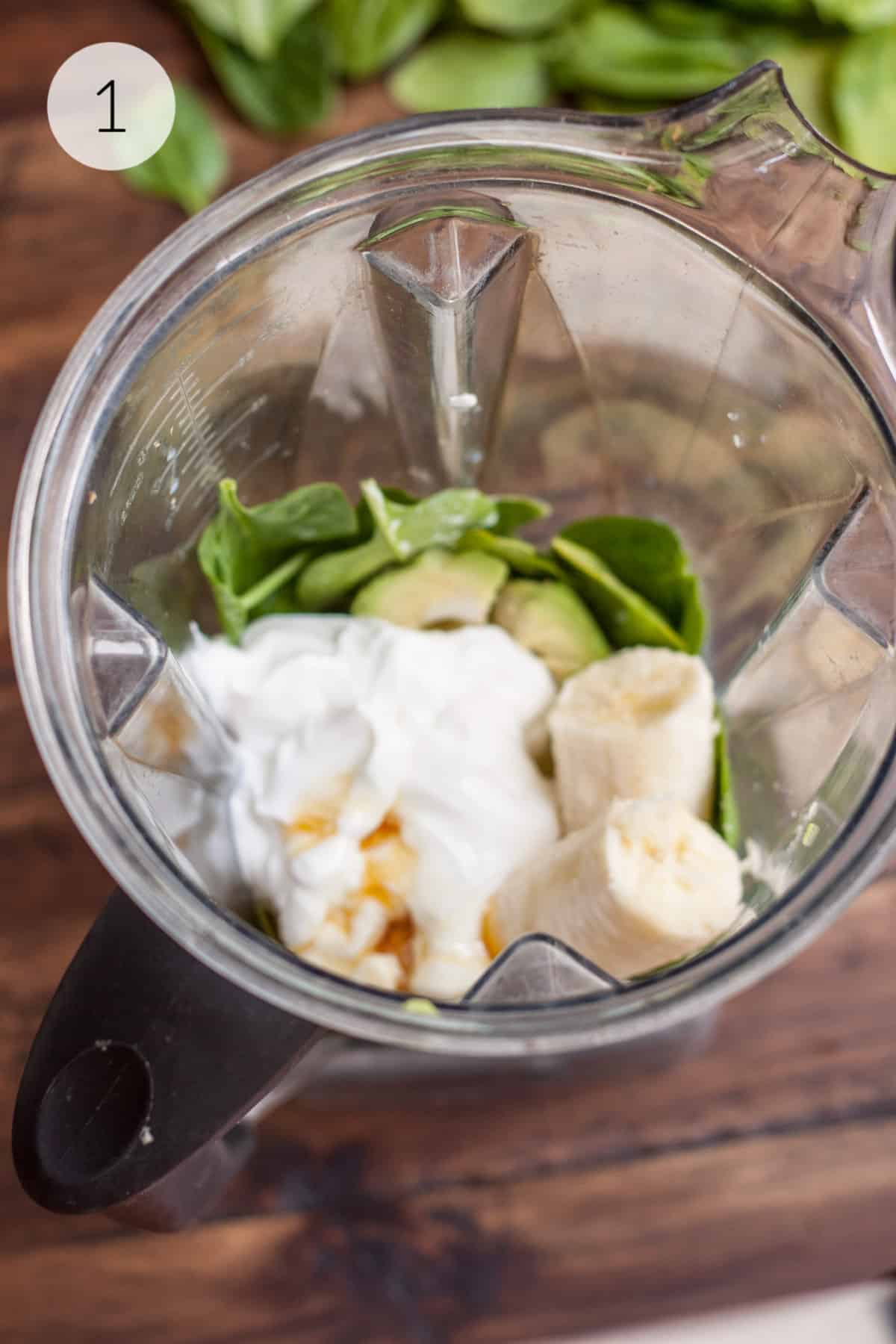Blender jar with yogurt, banana, spinach, honey and avocado for a smoothie.