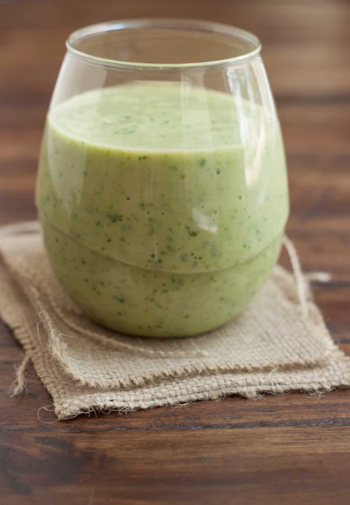 Clear glass with green banana spinach avocado smoothie on a brown burlap napkin.