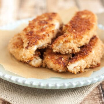 stack of coconut crusted chicken tenders on parchment paper on a blue plate and burlap napkin