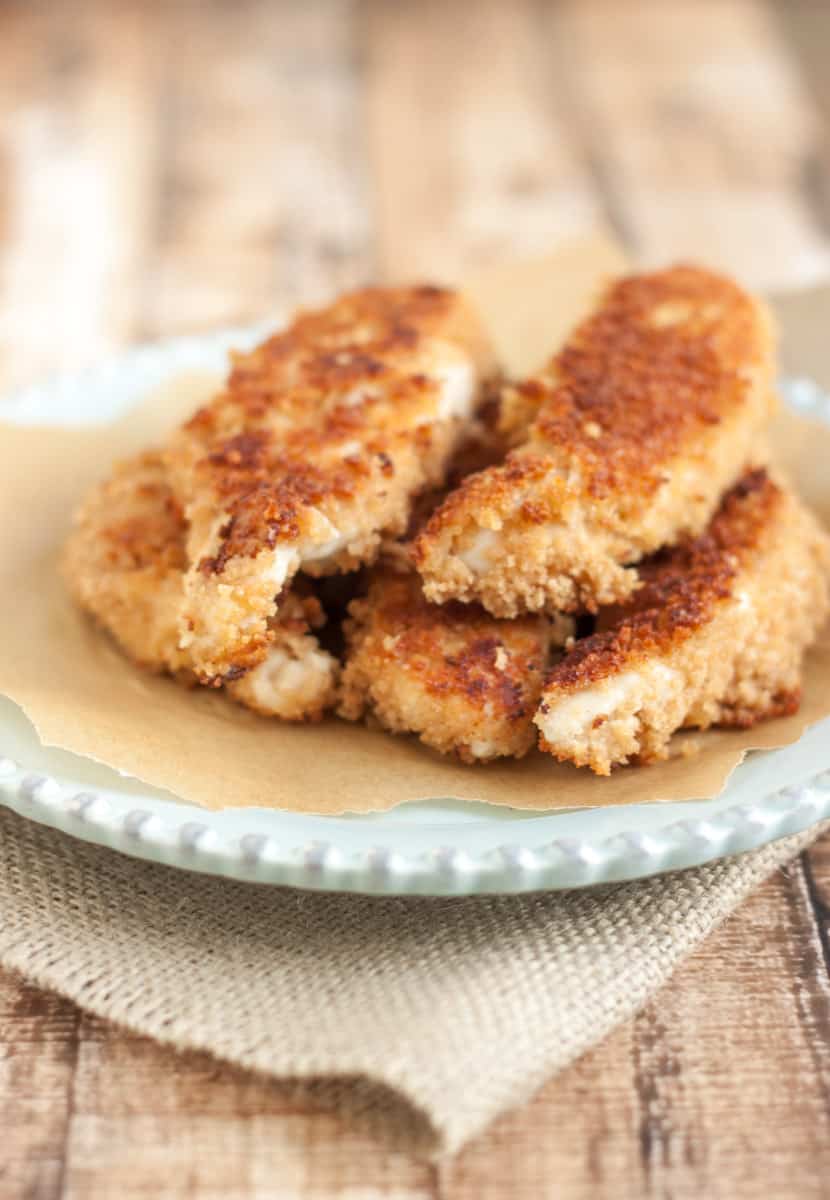 stack of coconut crusted chicken tenders on parchment paper on a blue plate and burlap napkin