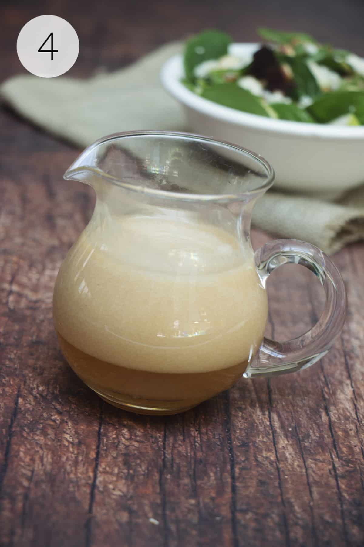 Small glass pitcher with Vidalia Onion Dressing in it and green leafy salad on napkin in background.