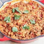 Spanish Rice with Ground Beef with cilantro sprigs in a red cast iron skillet on a cutting board.