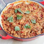 Red cast iron skillet with Spanish Rice with Ground Beef dish topped with cilantro leaves.