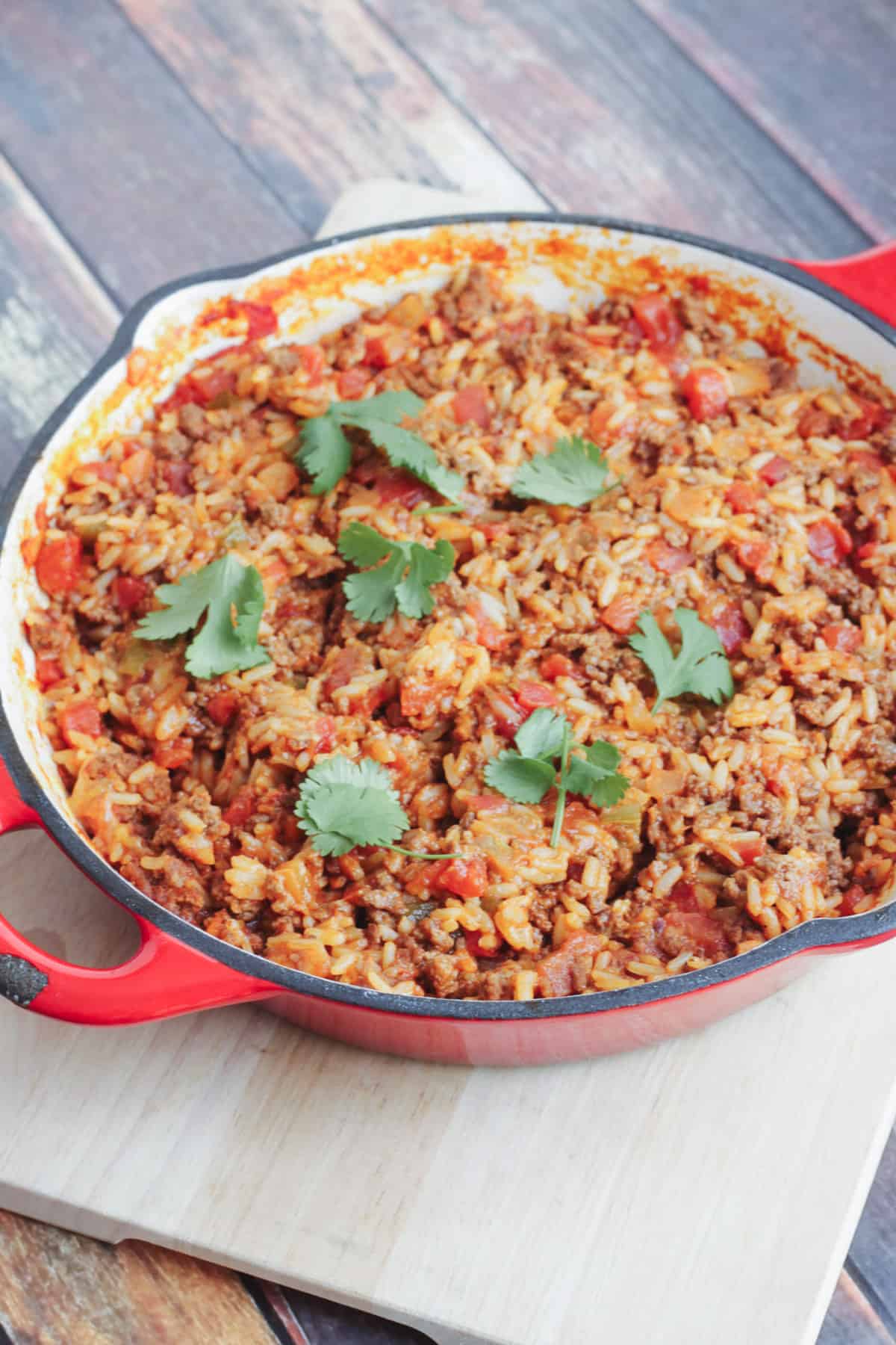 Red cast iron skillet with Spanish Rice With Ground Beef and cilantro leaves on top.