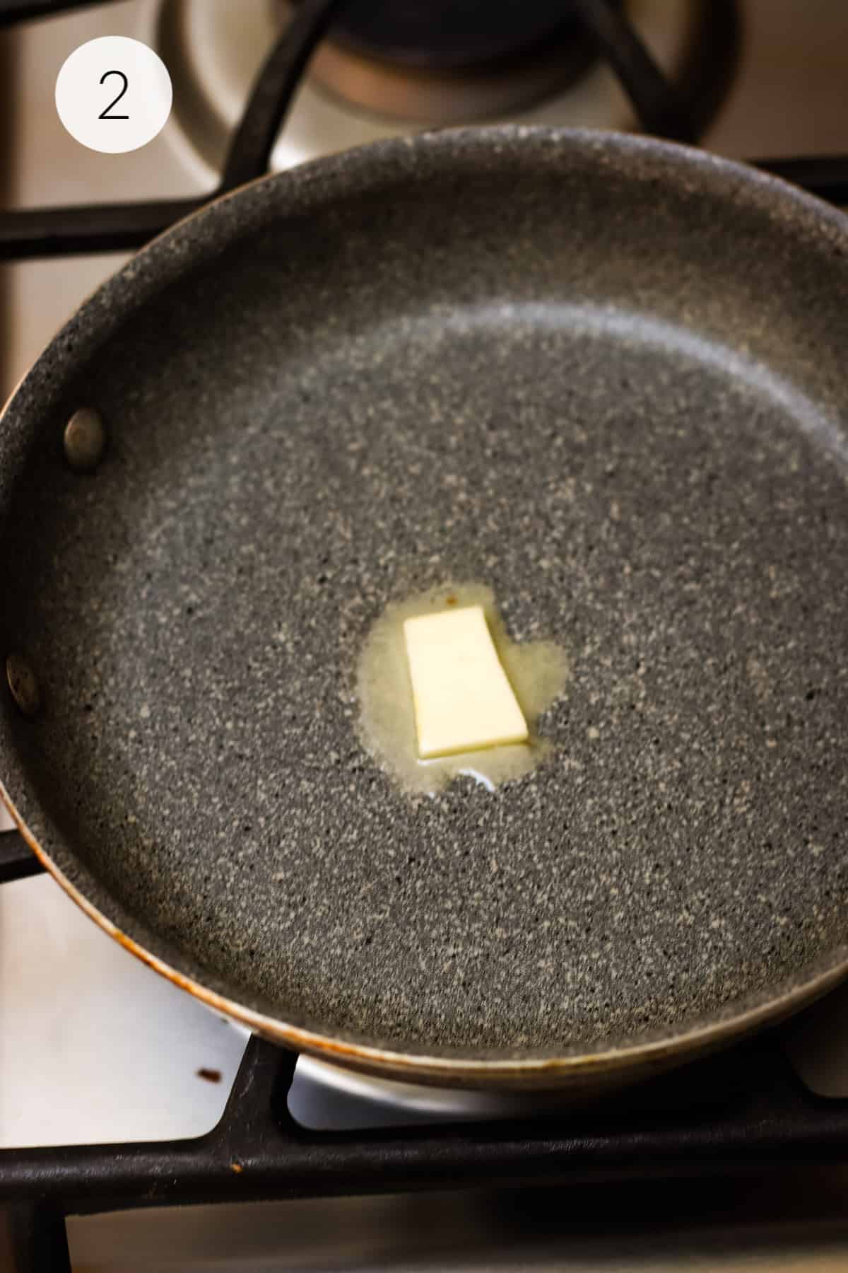 Small piece of butter melting in a grey saute pan. 