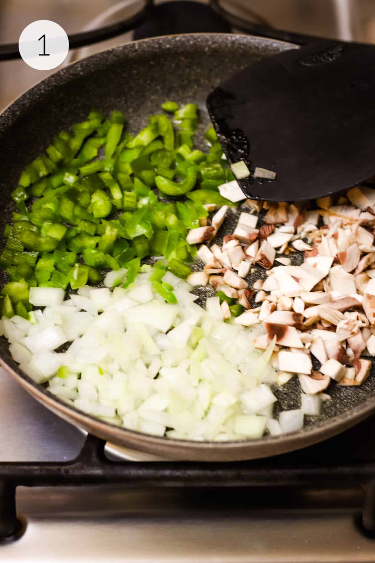 Chopped green bell peppers, mushrooms and onions sautéing  with a black spatula in pan.