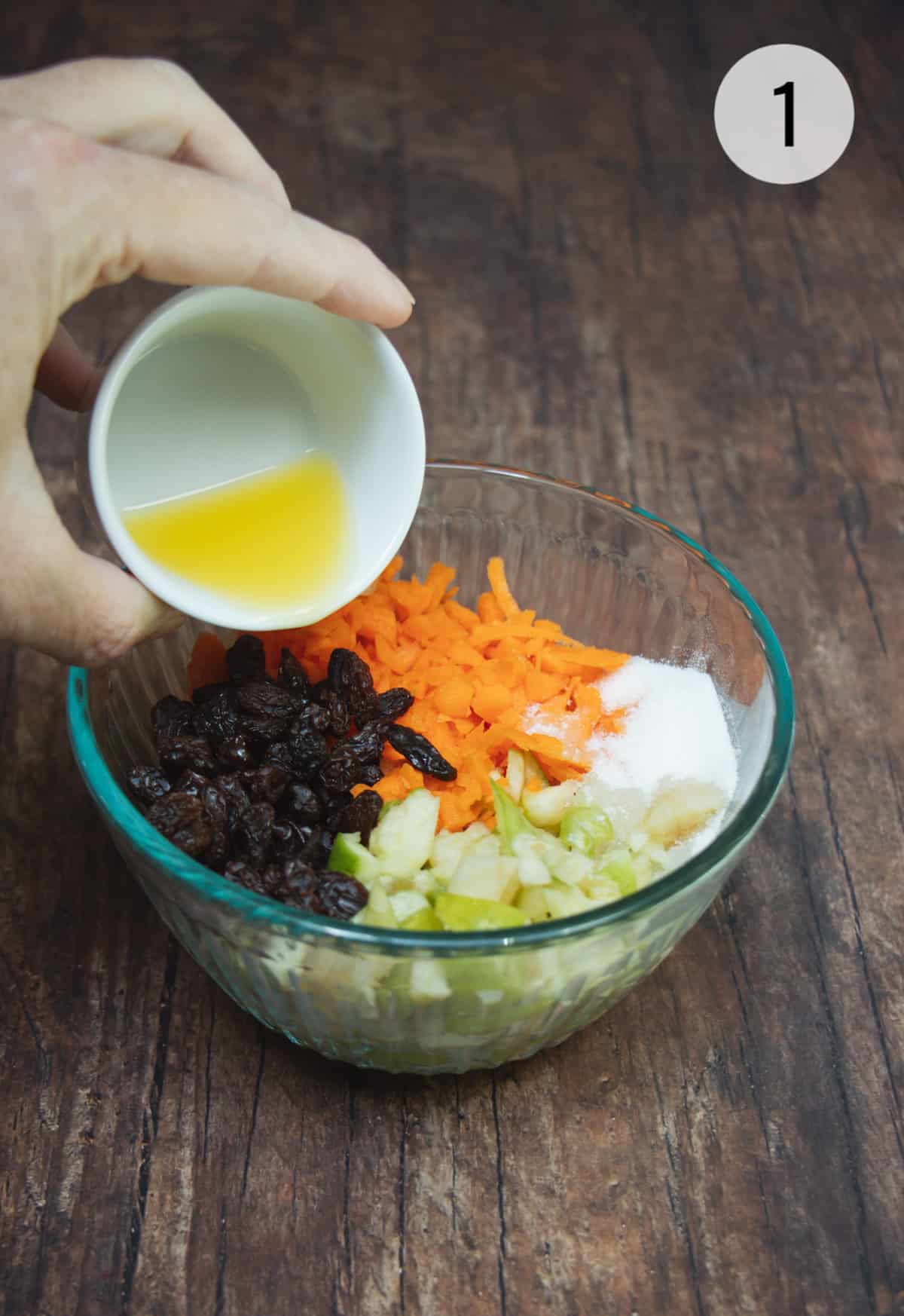Chopped apples and carrots with raisins and sugar in a small bowl with orange juice being poured in.