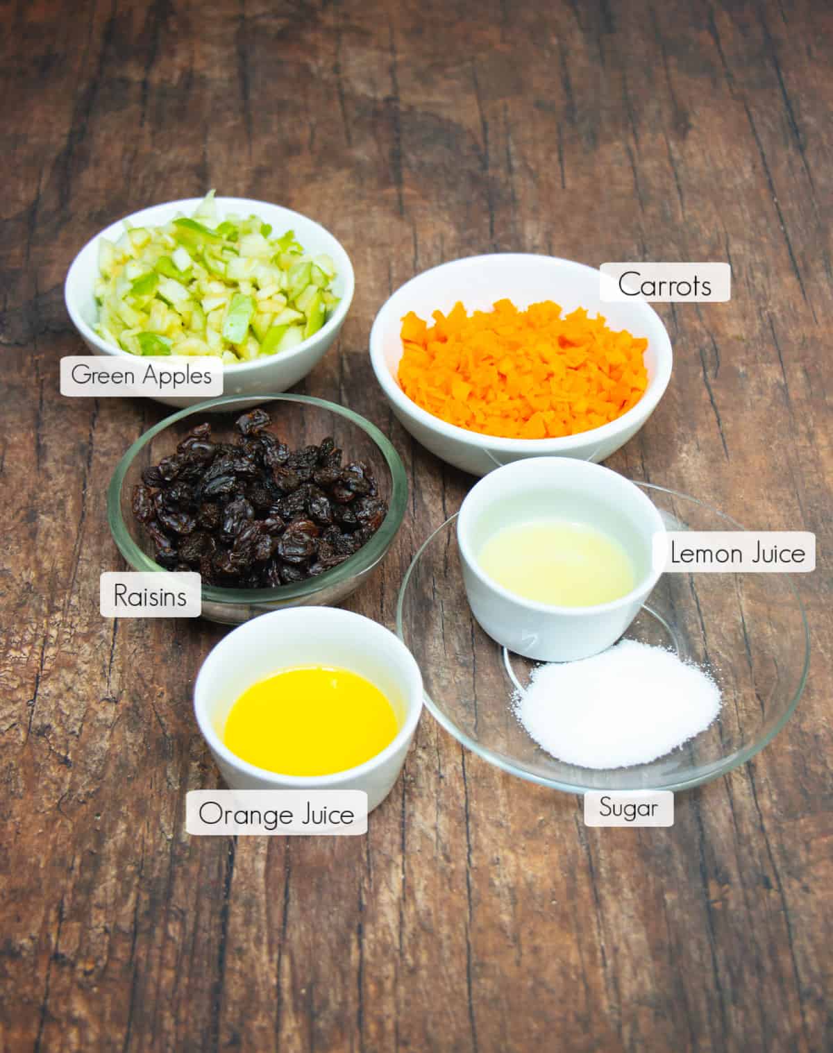 Ingredients in labeled bowls to make Apple Carrot Salad.