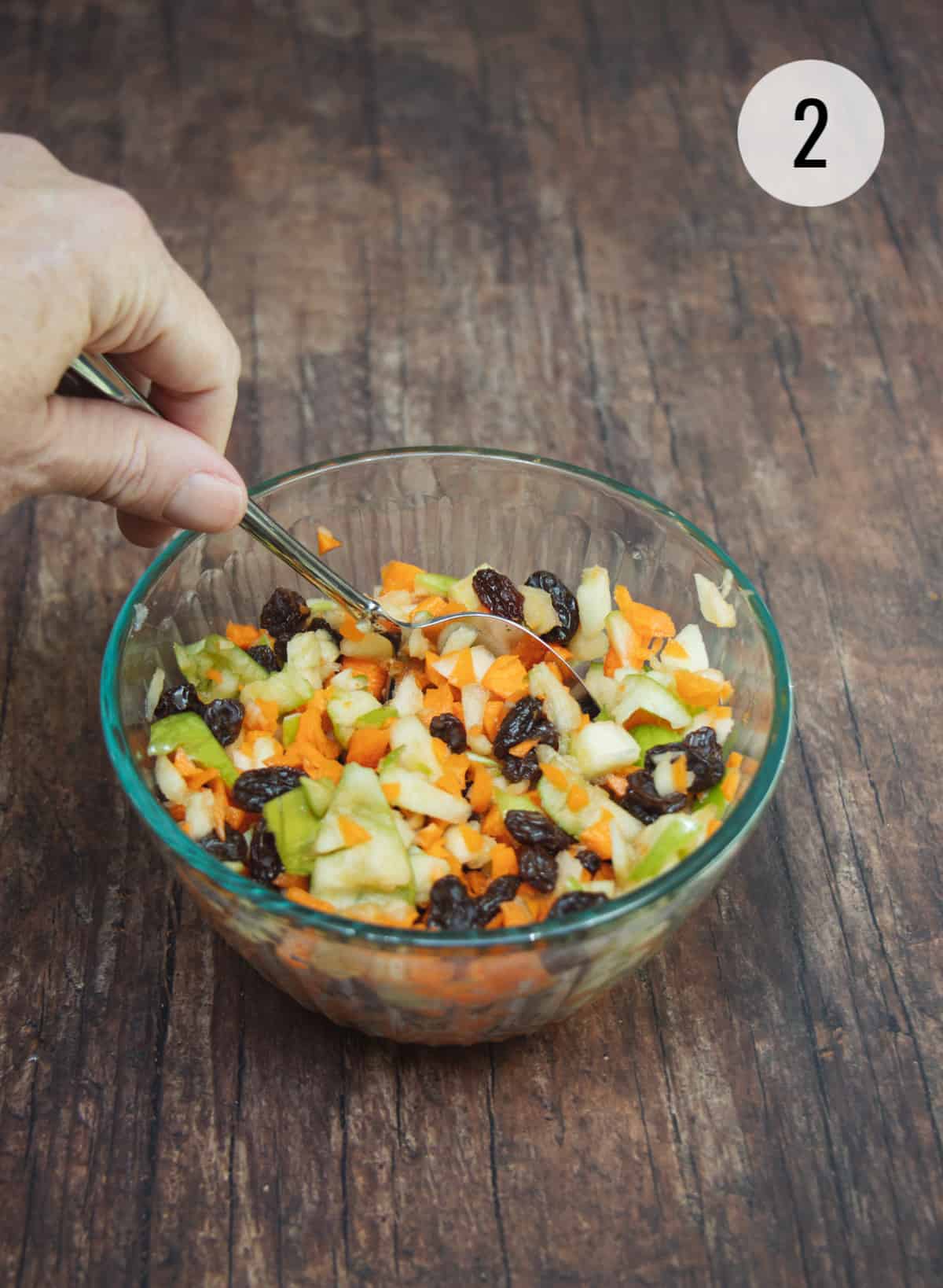 Stirring ingredients for Apple Carrot Salad with Raisins in a small bowl.